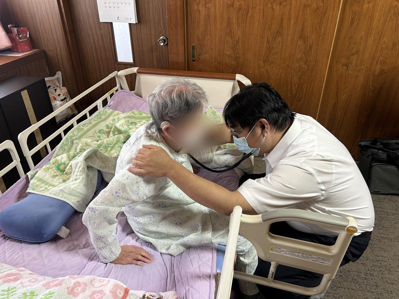 ご自宅の介護ベッドで療養する高齢の患者さんを、訪問診療の医師が聴診している様子